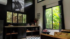 Una habitación con piso de estampado blanco y negro, un ventanal con vista a la vegetación, un sofá y un comedor con mesa y sillas negras.