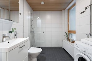 Casa de banho moderna com chuveiro, sanita, lavatório e máquina de lavar roupa embutida.