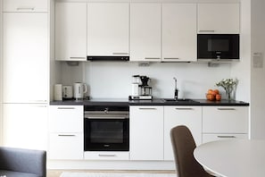 A modern kitchen with white cabinets, a black countertop, a built-in oven, a coffee maker, and a microwave. - Mall of Tripla apartment for 5 people / best loc. (Helsinki)