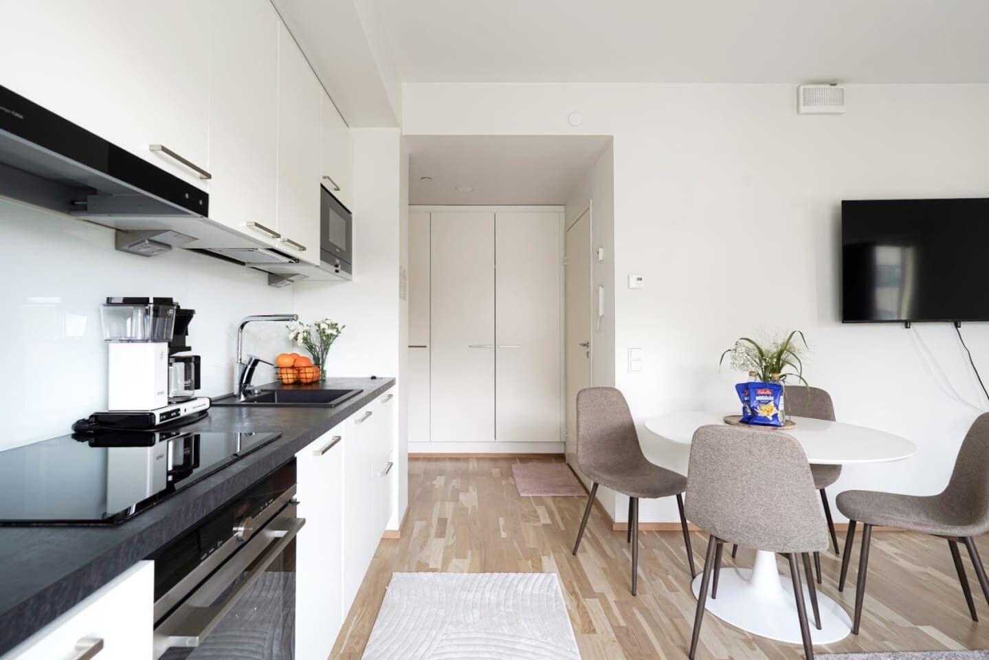 A modern kitchen with a built-in oven, a coffee machine, and a dining area with a round table and chairs.