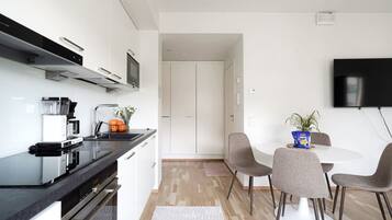A modern kitchen with a built-in oven, a coffee machine, and a dining area with a round table and chairs.