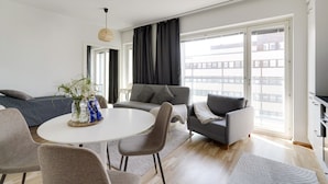 Un salon moderne avec une table à manger ronde, des canapés gris et une grande fenêtre donnant sur la ville.