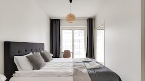 Une chambre d’hôtel moderne avec un grand lit, un luminaire suspendu et une vue sur les immeubles par la fenêtre.