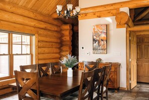 A wooden interior with a dining table, chairs, a chandelier, and a painting. - Log Cabin Getaway | Hot Tub | Ski, Hike, Relax (Silverthorne)