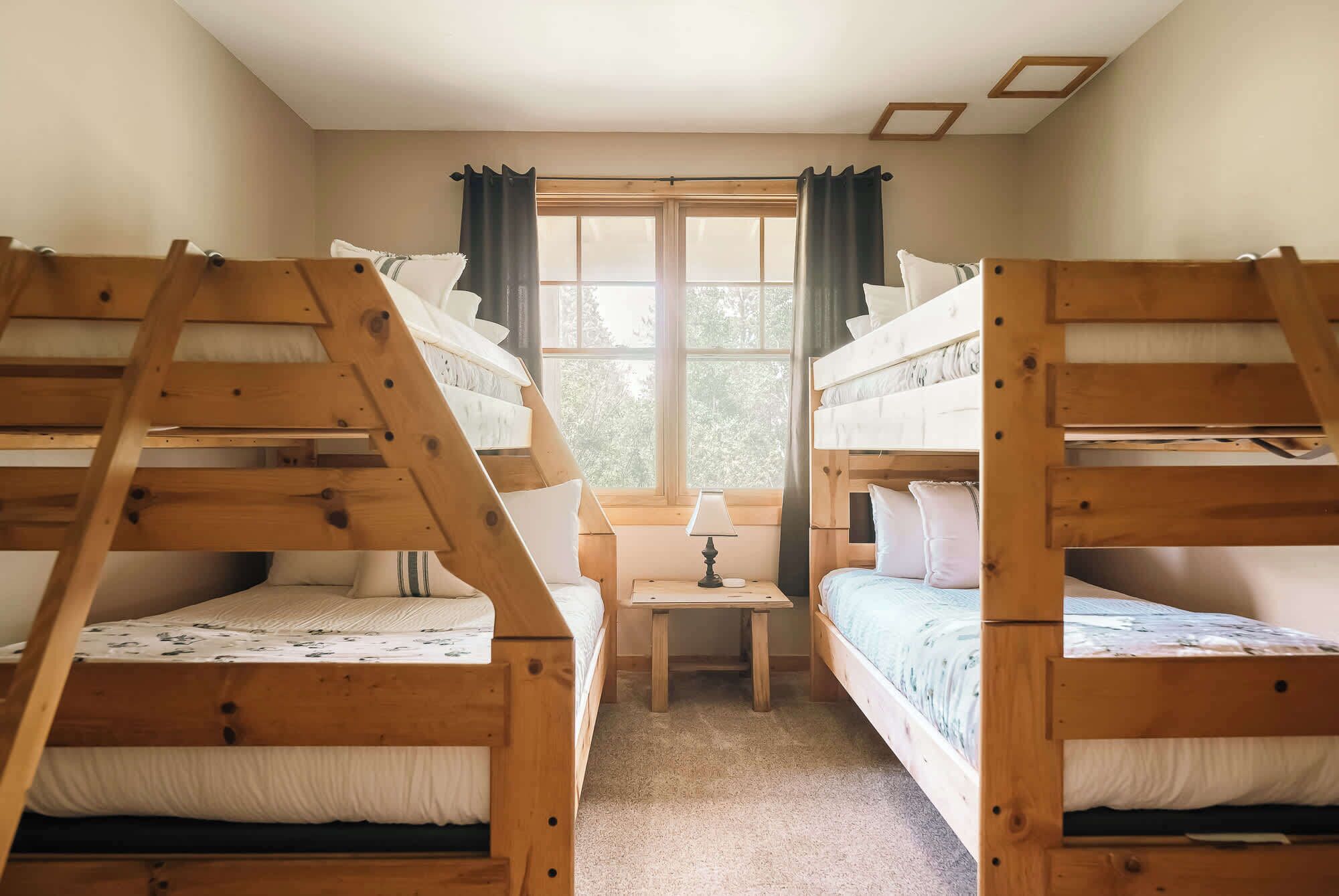 Een kamer met stapelbedden, een tafeltje met een lamp en een raam met gordijnen.
