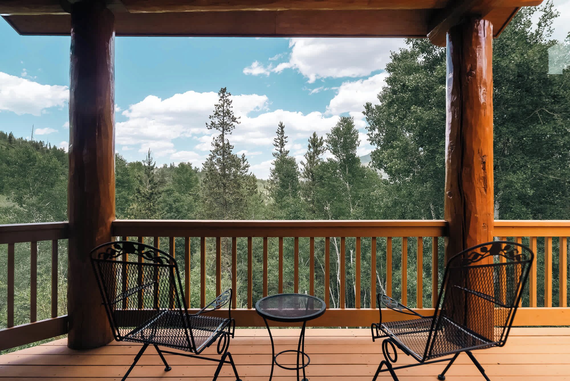 Eine Holzterrasse mit zwei Metallstühlen und einem kleinen Tisch, mit Blick auf ein bewaldetes Gebiet.