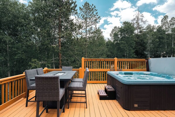 A wooden deck with outdoor furniture, a hot tub, and a view of trees.
