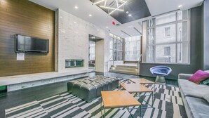 Un área de estar moderna con un televisor de pantalla plana, chimenea, asientos cómodos y ventanas amplias con vistas a la ciudad.