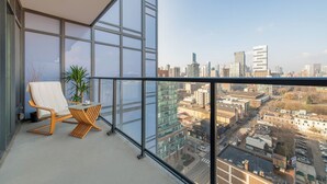 Un balcón con vista a la ciudad, una silla, una mesita y una planta en maceta.