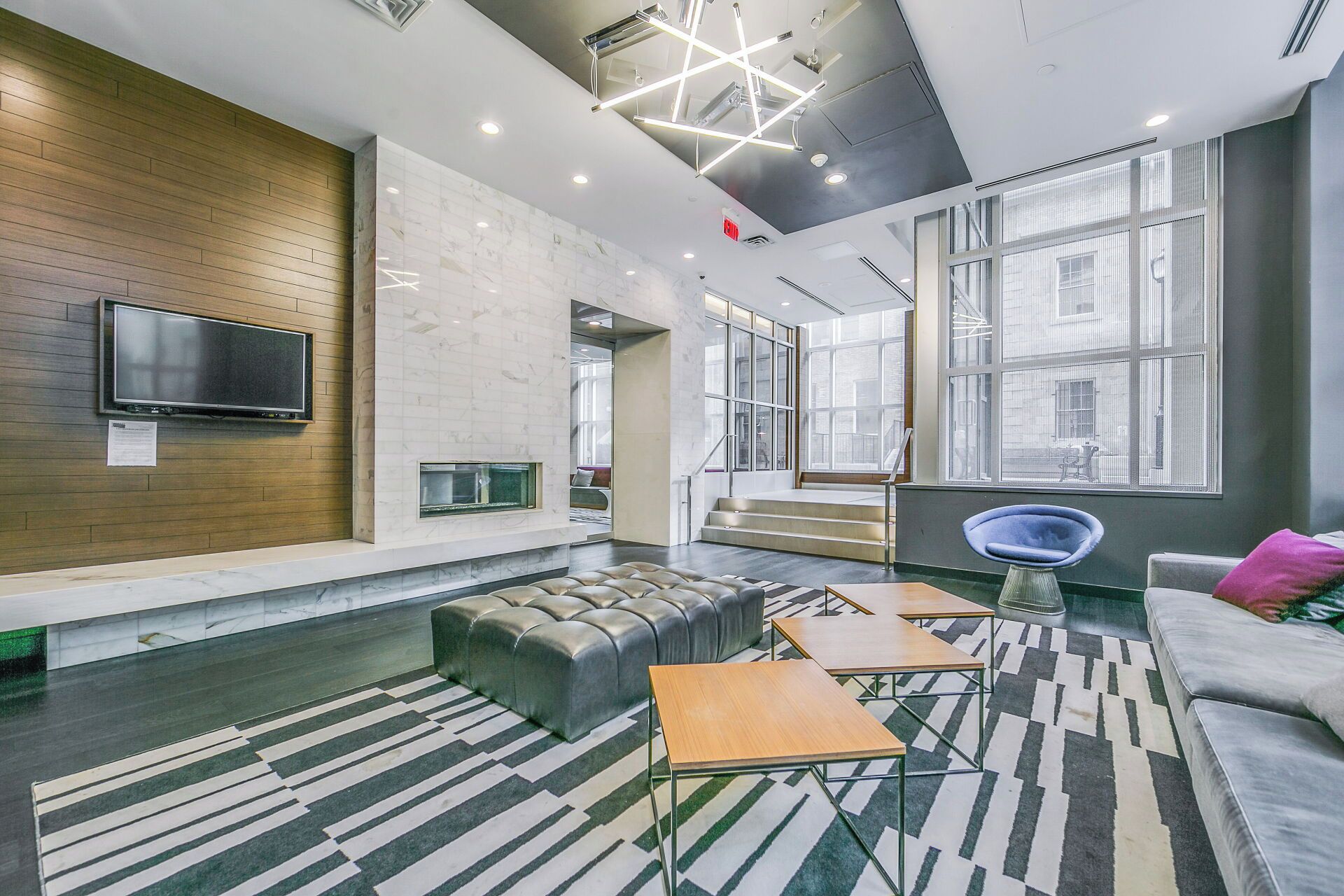 A modern lounge area with a flat-screen TV, a fireplace, comfortable seating, and large windows offering views of the city.