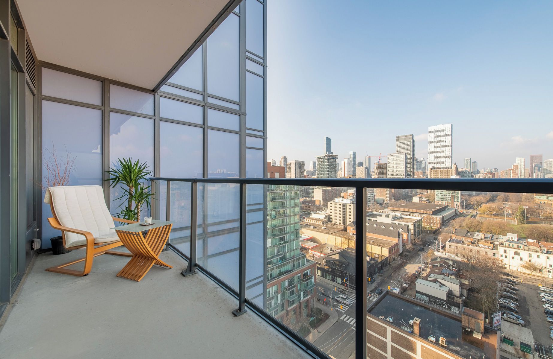 A balcony with a city view, a chair, a small table, and a potted plant.