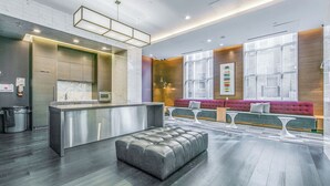 Un moderno vestíbulo de hotel con una zona de estar central, una kitchenette y un botiquín en la pared.