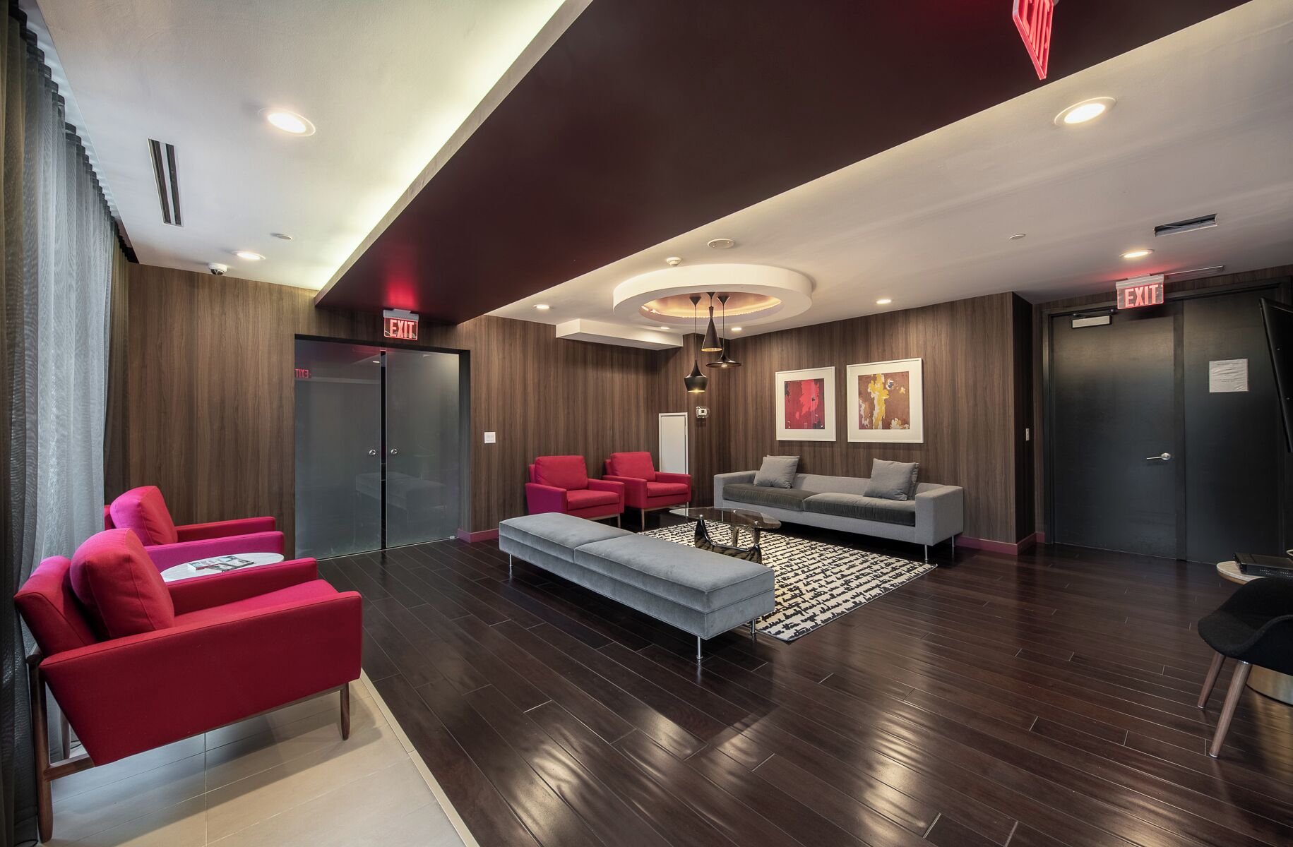 A modern lobby with a grey sofa, red chairs, a patterned rug, and wooden flooring.