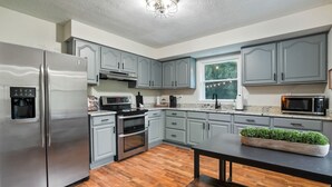 A modern kitchen with grey cabinets, stainless steel appliances, and a wooden floor.