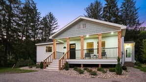 A two-story house with a covered porch, a staircase leading to the entrance, and a gravel driveway.