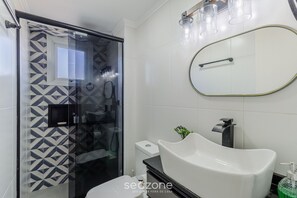 Un baño moderno con cabina de ducha de vidrio, un lavabo blanco y un espejo grande.