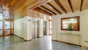 Un pasillo con vigas de madera en el techo, un ascensor, una mesa de vidrio con una planta y un espejo en un marco en la pared.