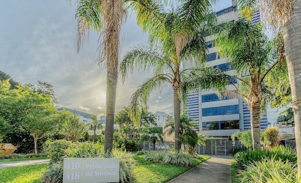 A sign for '410 Participado de Monaco' in a landscaped area with palm trees and a pathway leading to a modern building.