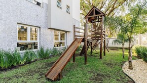 A modern building with a white exterior and a wooden play structure with a slide. - Cozy and Well-located Apartment in POA - Rfa303 (Porto Alegre)