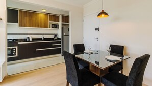A modern kitchen with black and white cabinetry, a microwave, and a refrigerator. There is a dining table with four chairs and a hanging pendant light. - Cozy and Well-located Apartment in POA - Rfa303 (Porto Alegre)