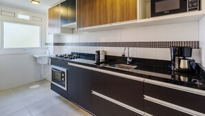 A modern kitchen with dark cabinetry, a black countertop, a built-in microwave, and a coffee maker. - Cozy and Well-located Apartment in POA - Rfa303 (Porto Alegre)