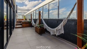 A rooftop terrace with large windows, a hammock, and potted plants. - Lindo Apto em Cond. c\/ Piscina e Garagem RPF0605 (Porto Alegre)