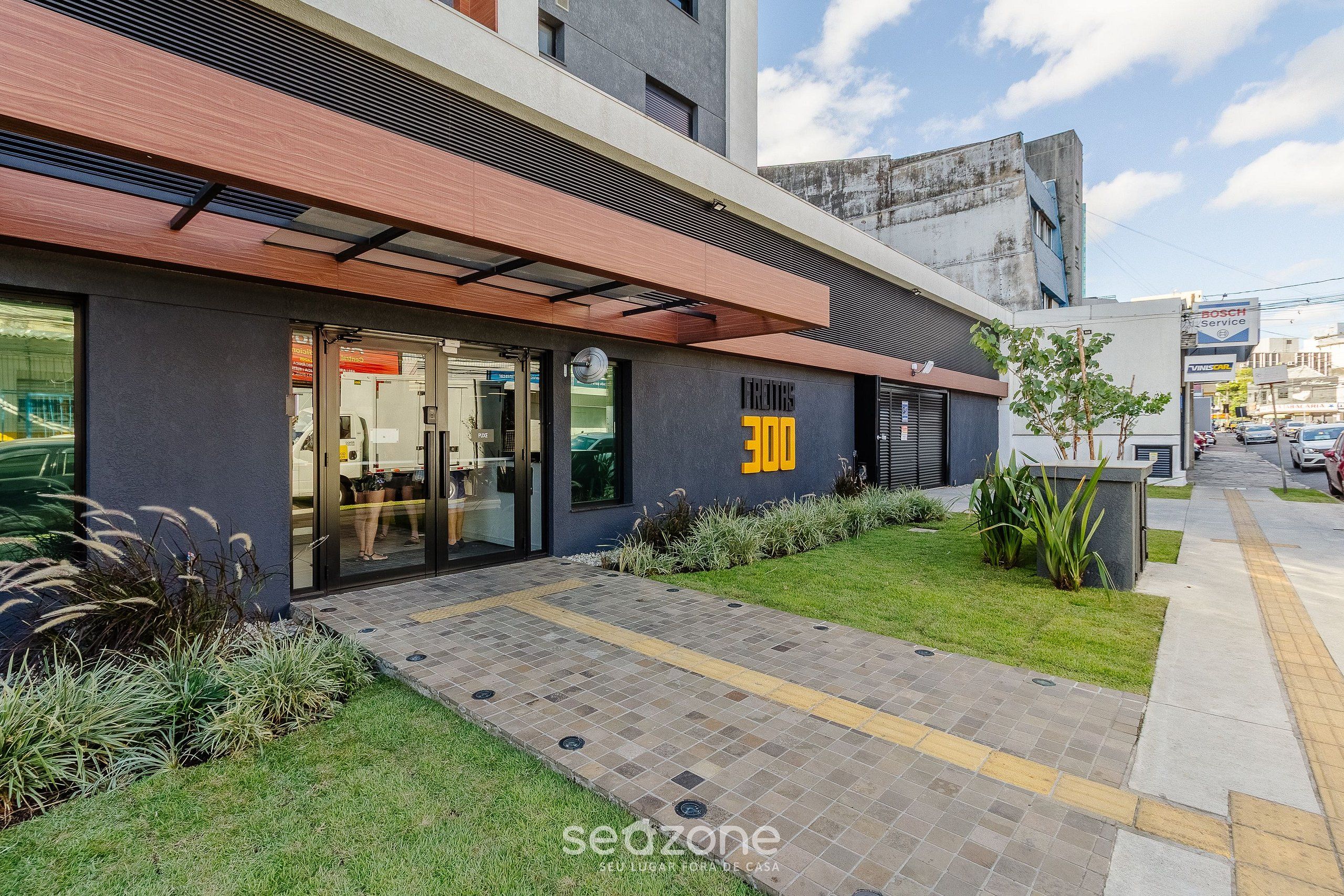 A modern building with a glass entrance, a sign reading "300", and a small garden area.