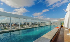 A rooftop infinity pool with a city view, surrounded by glass railings and wooden decking. - Lindo Apto em Cond. c\/ Piscina e Garagem RPF0605 (Porto Alegre)