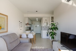 A modern living room with a sofa, TV, and dining area. - Lindo Apto em Cond. c\/ Piscina e Garagem RPF0605 (Porto Alegre)