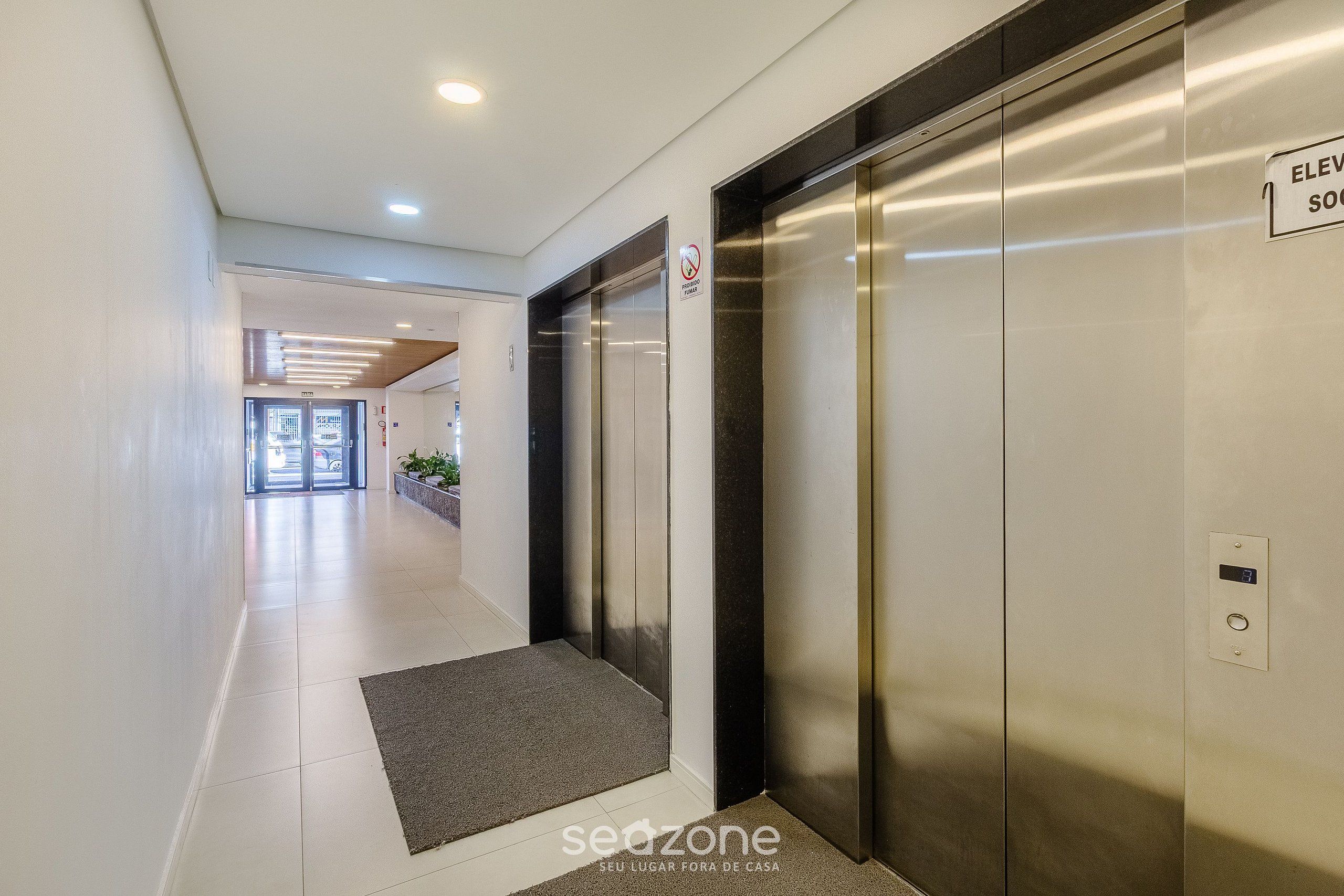 A modern hallway with two elevators, a digital display, and a no-smoking sign.