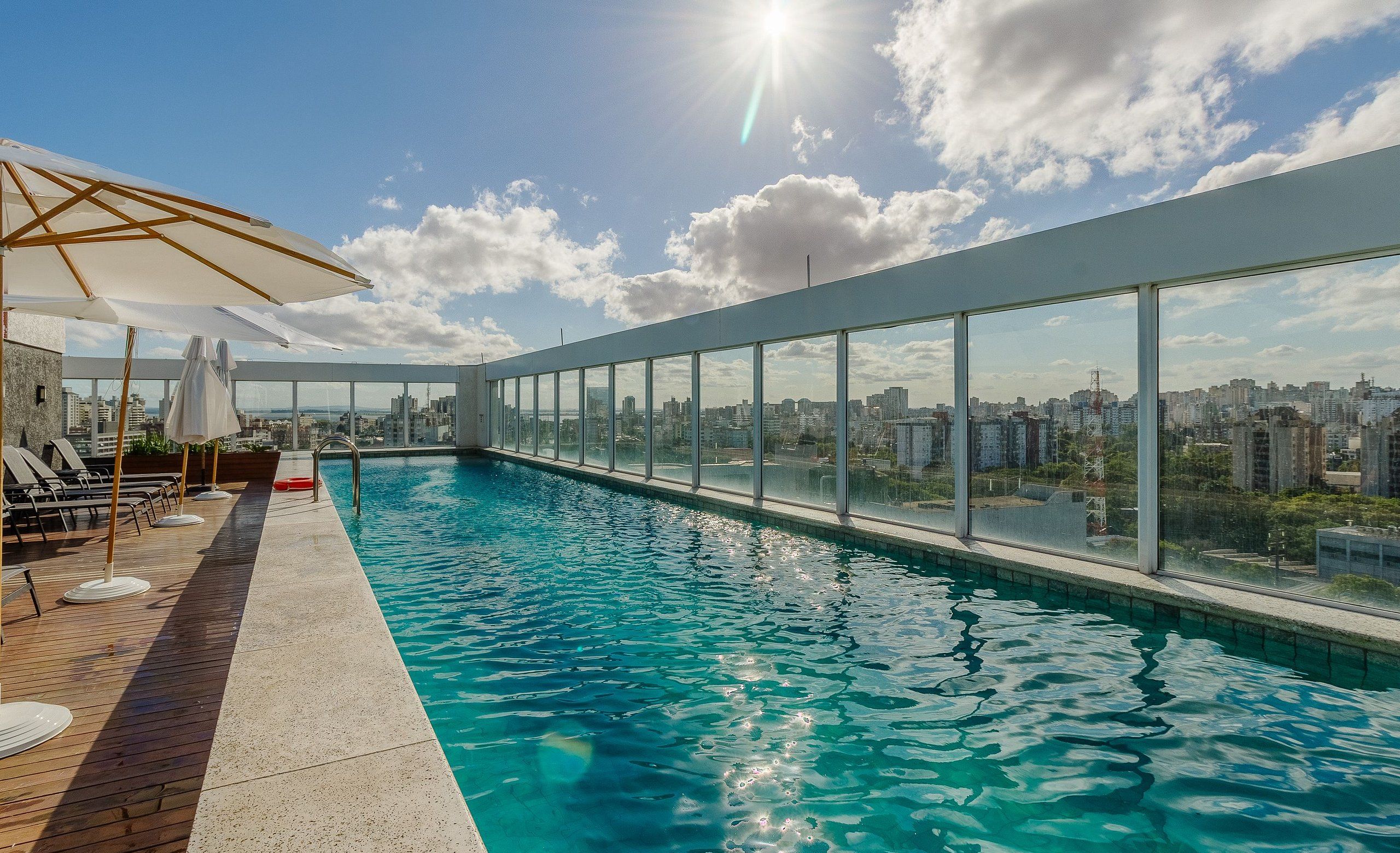 A rooftop swimming pool with clear blue water, surrounded by lounge chairs and umbrellas, offering a city view.