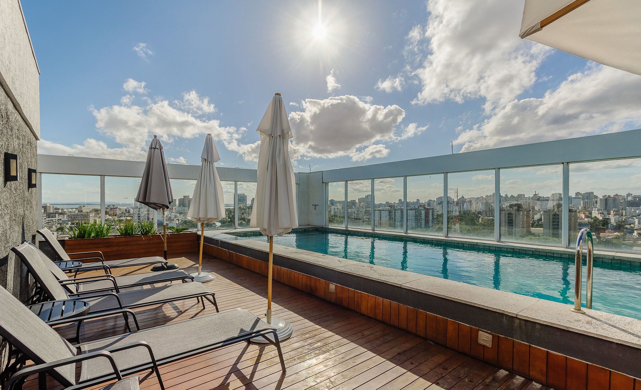 A rooftop pool area with lounge chairs and umbrellas, overlooking a cityscape.