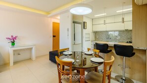 A modern dining area with a glass table, wooden chairs, and a pendant light. - Beautiful Apartment With Barbecue in PoA Rps0460 (Porto Alegre)