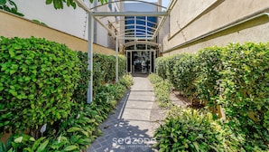 A covered pathway flanked by lush greenery leading to a building entrance. - Beautiful Apartment With Barbecue in PoA Rps0460 (Porto Alegre)