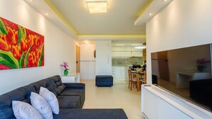 A modern living room with a sofa, a flat-screen TV, and a vibrant painting on the wall. - Beautiful Apartment With Barbecue in PoA Rps0460 (Porto Alegre)