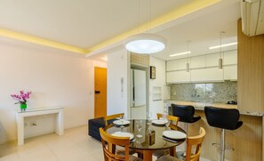 Uma sala de jantar moderna com mesa de vidro, cadeiras de madeira e uma luminária pendente.