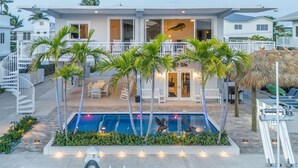 A modern two-story house with a swimming pool, outdoor seating, and a thatched roof structure. - Beautiful two- story beach house (Islamorada)