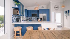 A modern kitchen with blue cabinets, a white countertop, and a wooden dining table. - Beautiful two- story beach house (Islamorada)