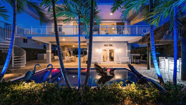 A two-story building with a pool, palm trees, and outdoor seating. - Beautiful two- story beach house (Islamorada)