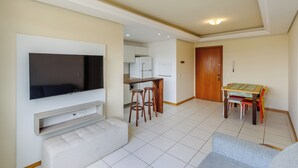 A modern living room with a flat-screen TV, a sofa, a dining area with a table and chairs, and a kitchen in the background. - Elegant Apartment for Couples in Poa-rs Urb1110 (Porto Alegre)