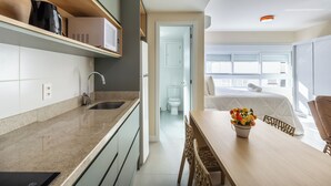 Une cuisine moderne équipée d’un évier, d’un four à micro-ondes et de placards, un coin repas avec une table et des chaises, et une chambre avec un lit et une fenêtre.