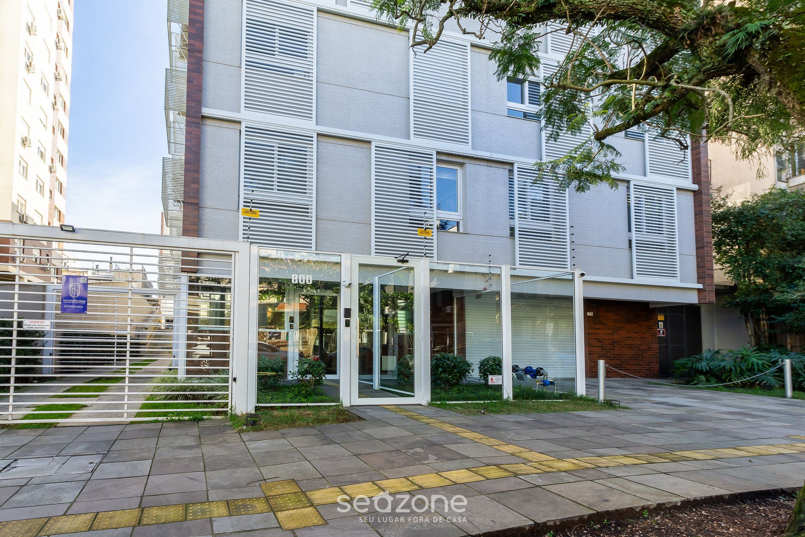 A modern building with a gated entrance, a covered outdoor area, and a paved walkway.