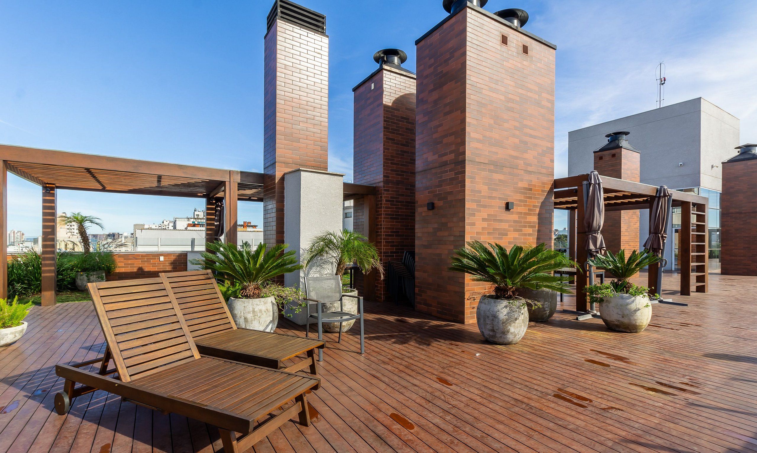 A rooftop terrace with wooden lounge chairs, potted plants, and a pergola.