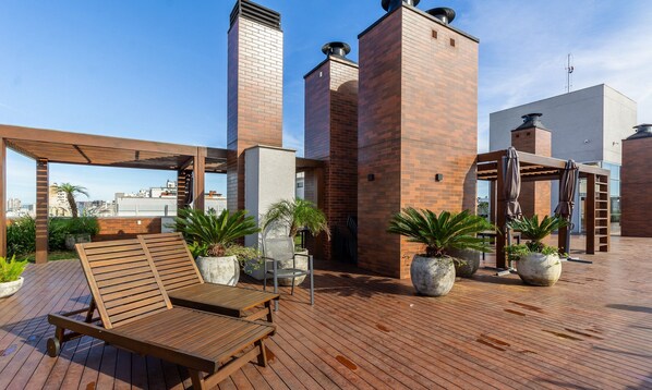 A rooftop terrace with wooden lounge chairs, potted plants, and a pergola.