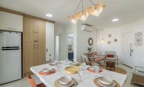 A modern kitchen with white cabinets, a built-in refrigerator, and a dining area with a white table set for six. - Apart With Barbecue 550m From the Beach Ups1002 (Porto Belo)
