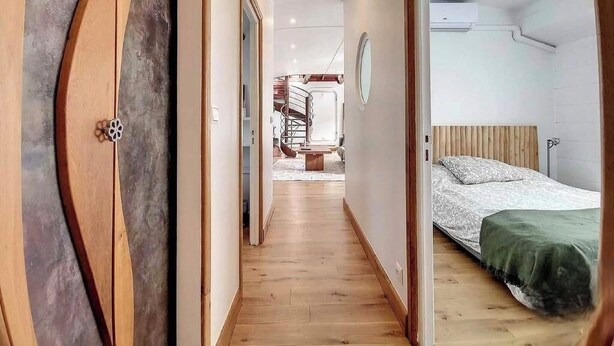A hallway leading to a bedroom with a bed, a wooden floor, and a staircase in the background. - Maison sur l'eau 3 chambres & Terrasse Proche Paris center (Villeneuve-la-Garenne)