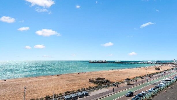A beach with a pier, a parking area, and a road with cars.