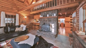 A log cabin interior with a stone fireplace, wooden furniture, and a cozy seating area.