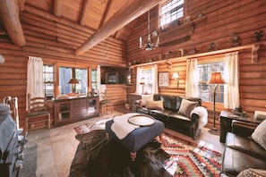 A log cabin interior with a fireplace, wooden furniture, and a large window.