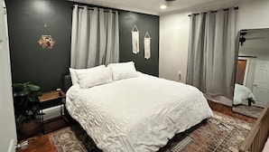 Ein Schlafzimmer mit einem großen Bett, einem Deckenventilator, einem Nachttisch, einem Spiegel und einem gemusterten Teppich.